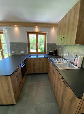Une cuisine moderne avec des meubles en bois, un plan de travail noir, un évier encastré et une fenêtre donnant sur un paysage verdoyant.