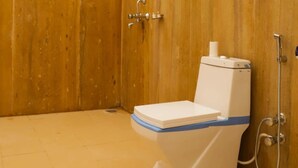 A small, wooden-walled bathroom with a toilet, a shower, and a white umbrella overhead. - Gujarat Resort Jaisalmer (Jaisalmer)