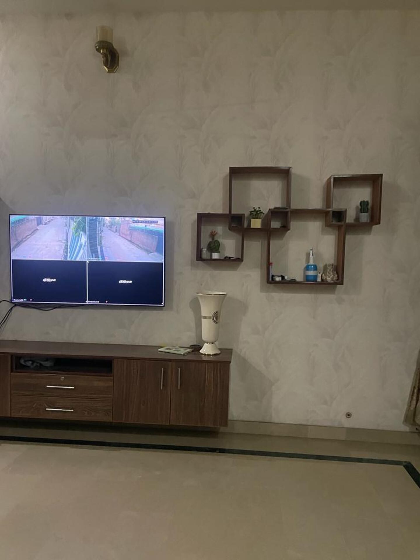 Un salon doté d’un téléviseur à écran plat fixé au mur, d’un meuble en bois avec des tiroirs et d’étagères murales ornées d’objets décoratifs.