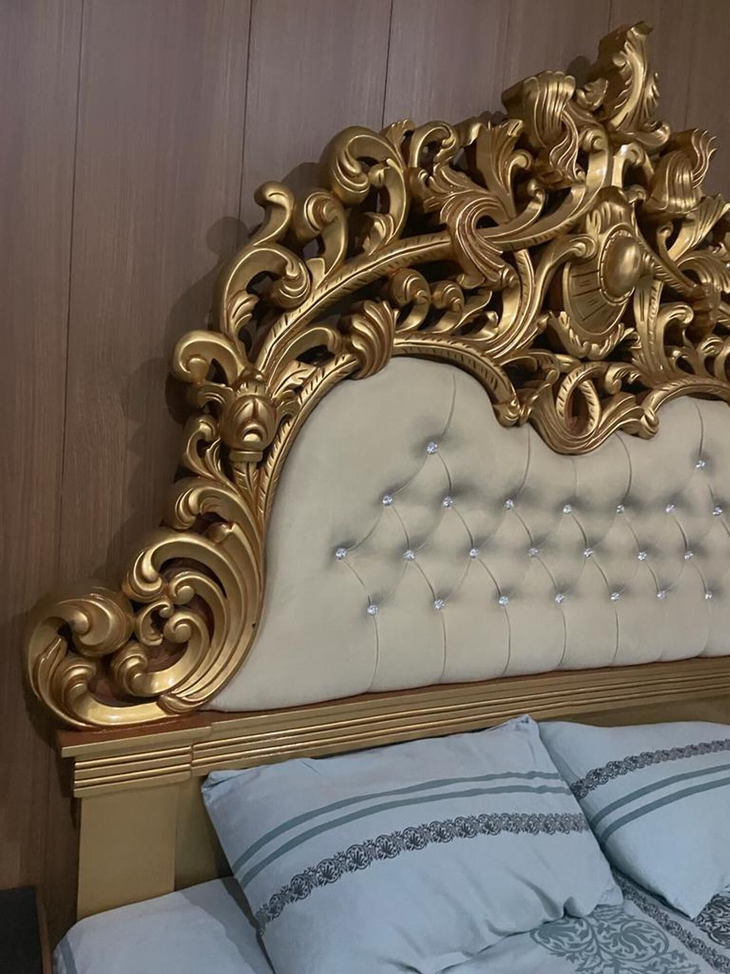 Una cama con cabecera capitonada y detalles decorativos tallados.