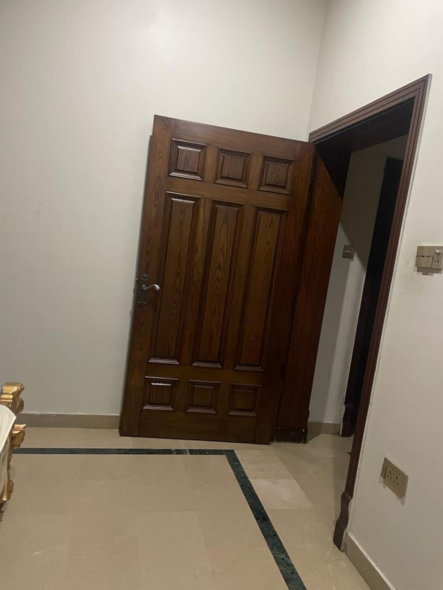 A wooden door with a panel design, a tiled floor with a dark border, and a light switch on the wall.