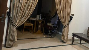 Una habitación con una puerta que presenta un diseño ornamental en negro y dorado, una pequeña mesa con una silla, y una mesa de vidrio al frente.