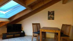 A cozy attic room with a skylight, wooden furniture, and a television.