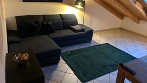A living room with a dark blue sectional sofa, a green rug, a small table with a decorative item, a floor lamp, and a painting on the wall.