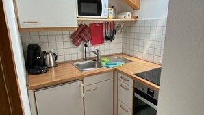 A compact kitchen with a microwave, kettle, and oven. It features a skylight and tiled flooring.