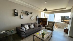 Ein modernes Wohnzimmer mit grauem Sofa, einem Glastisch und einem an der Wand montierten Fernseher.
