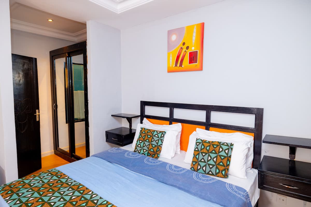 A bedroom with a bed, nightstands, a wall art piece, and a door.