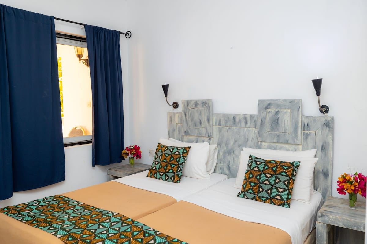 A double bed with patterned bedding, a headboard with a textured design, and two wall-mounted lamps.