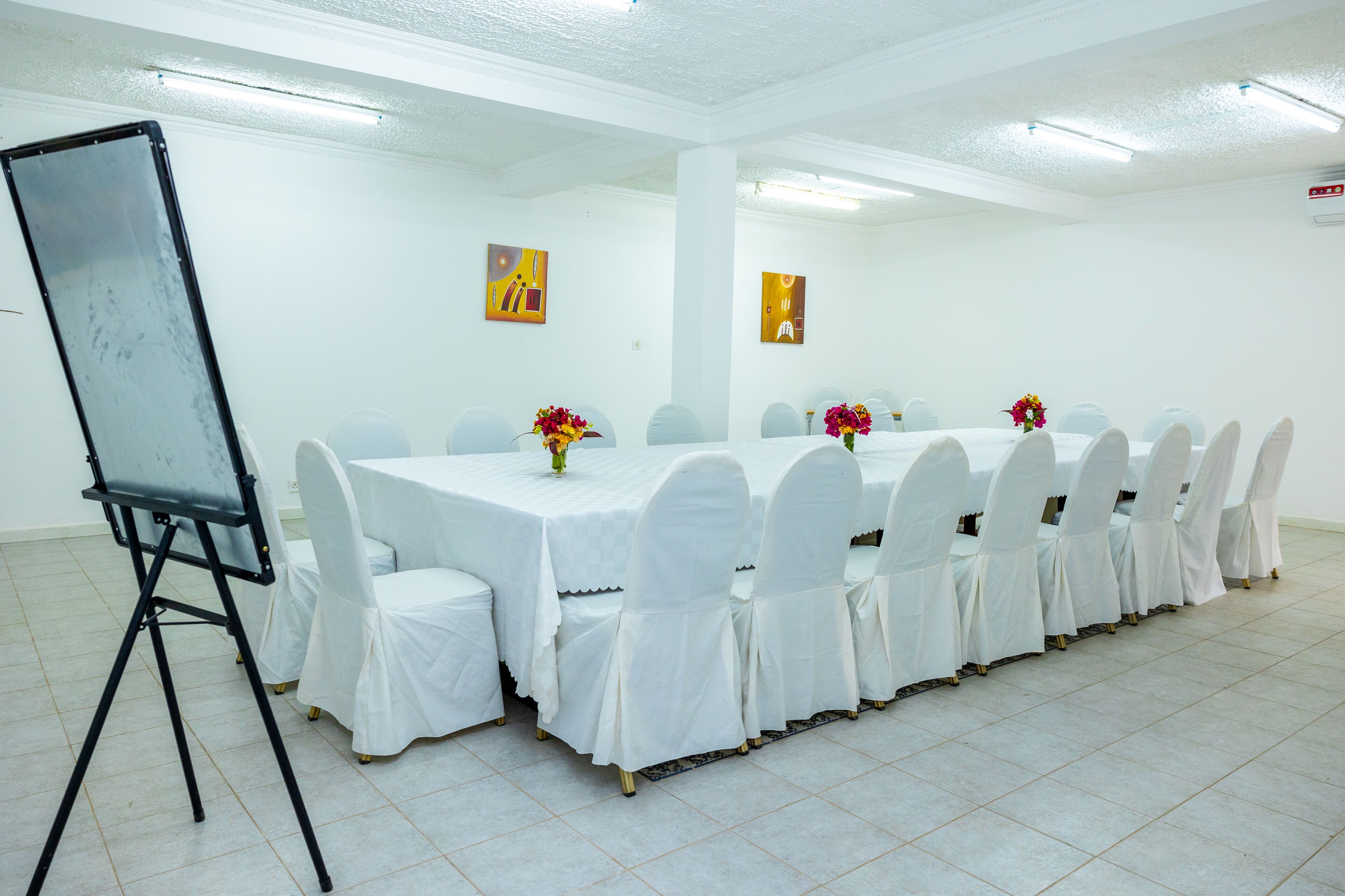 A conference room with a long table, white chairs, and a projector screen.