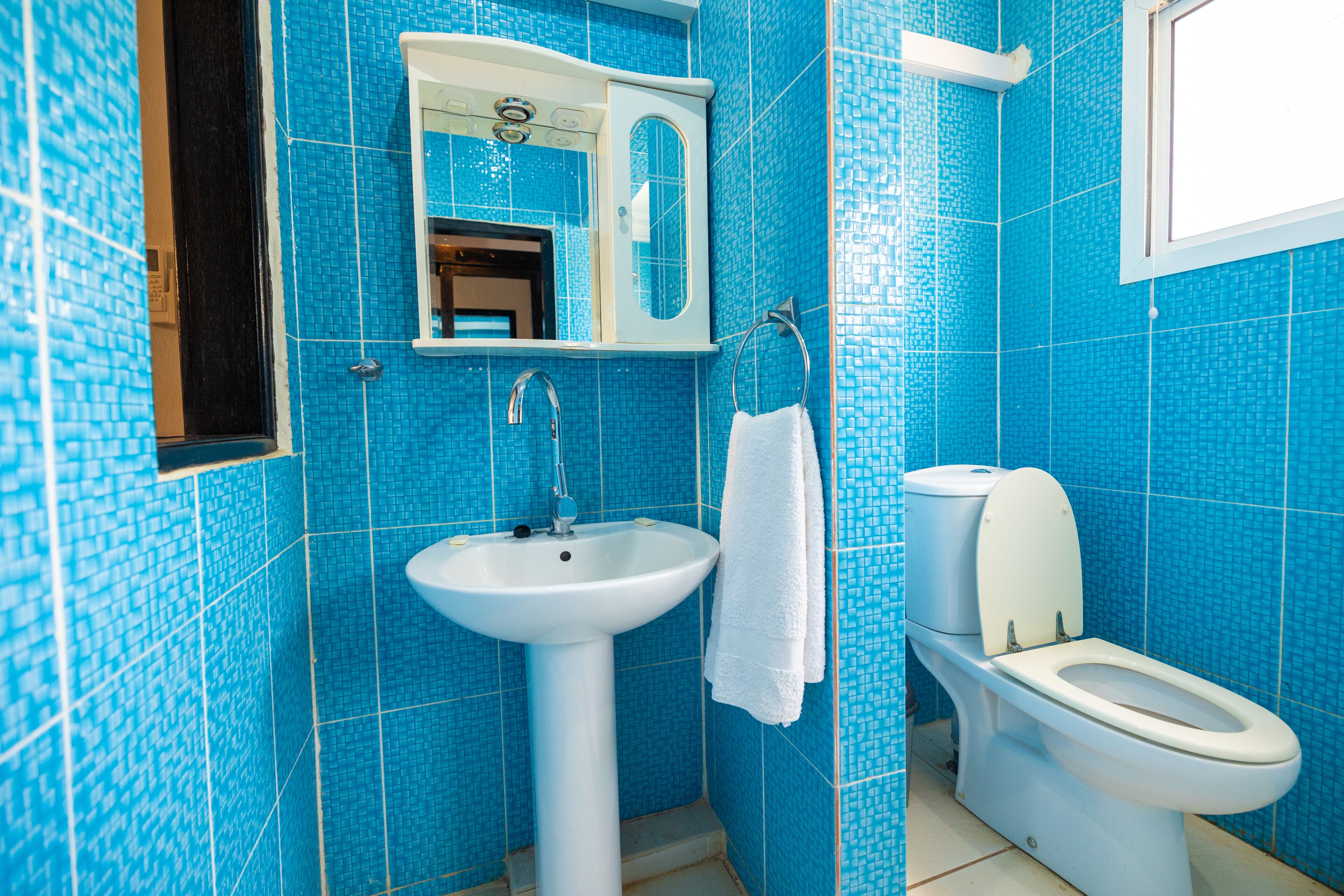 A bathroom with blue mosaic tiles, a white sink, a mirror, and a toilet.