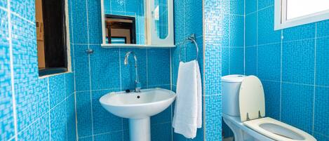 Een badkamer met blauwe mozaïektegels, een witte wastafel, een spiegel en een toilet.