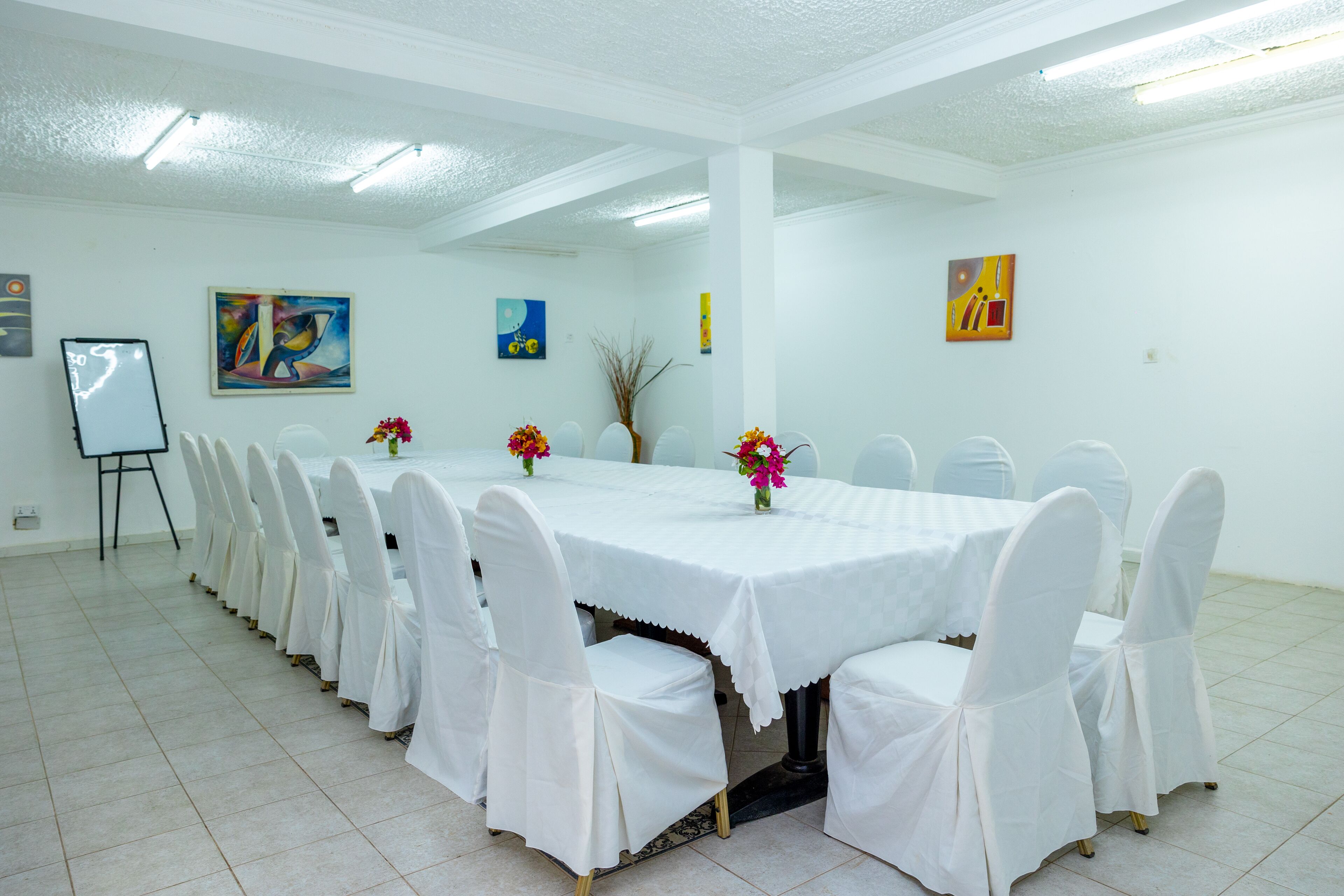 A conference room with a long table, white chairs, and floral centerpieces.