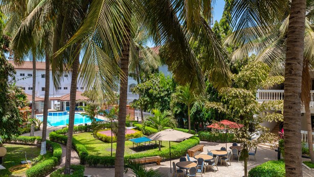 A resort courtyard with a pool, palm trees, and outdoor seating areas. - Sarge's Hotel (Serrekunda)