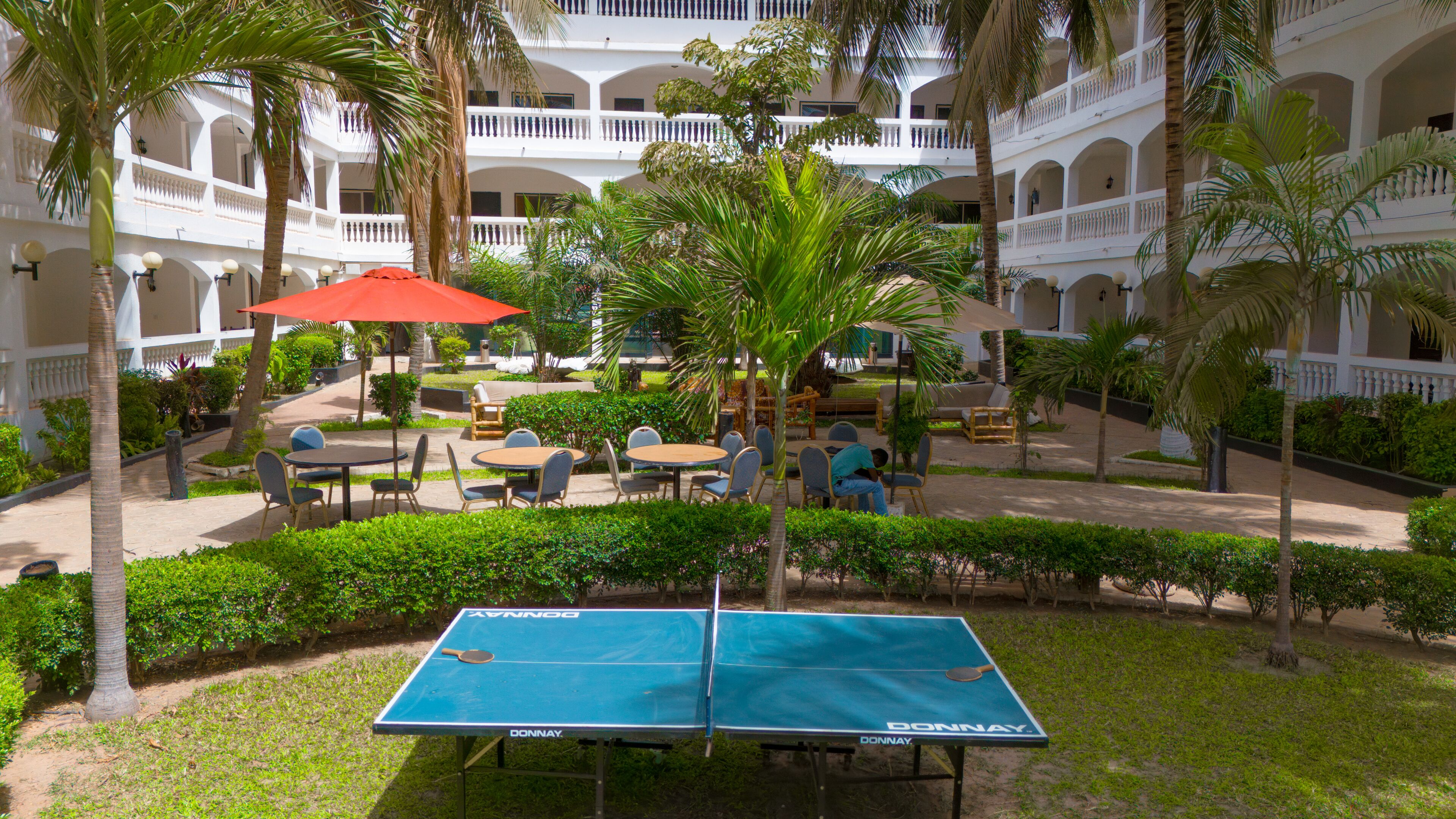 An outdoor courtyard with a ping pong table, seating area, and palm trees.