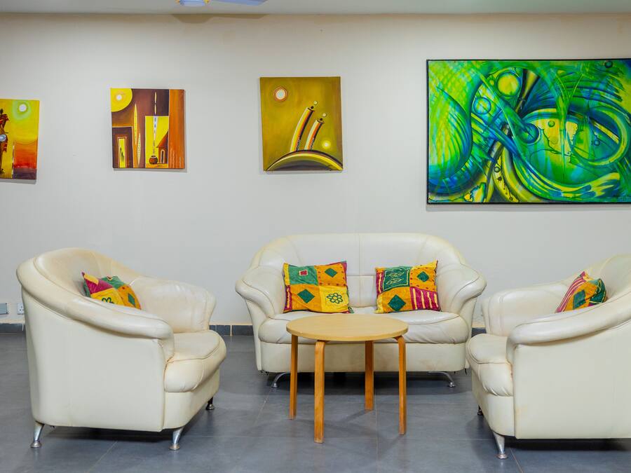 Une pièce comprenant trois canapés en cuir blanc, une table basse en bois et trois tableaux abstraits accrochés au mur.