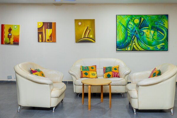Una habitación con tres sofás de cuero blanco, una mesa de centro de madera y tres cuadros abstractos en la pared.