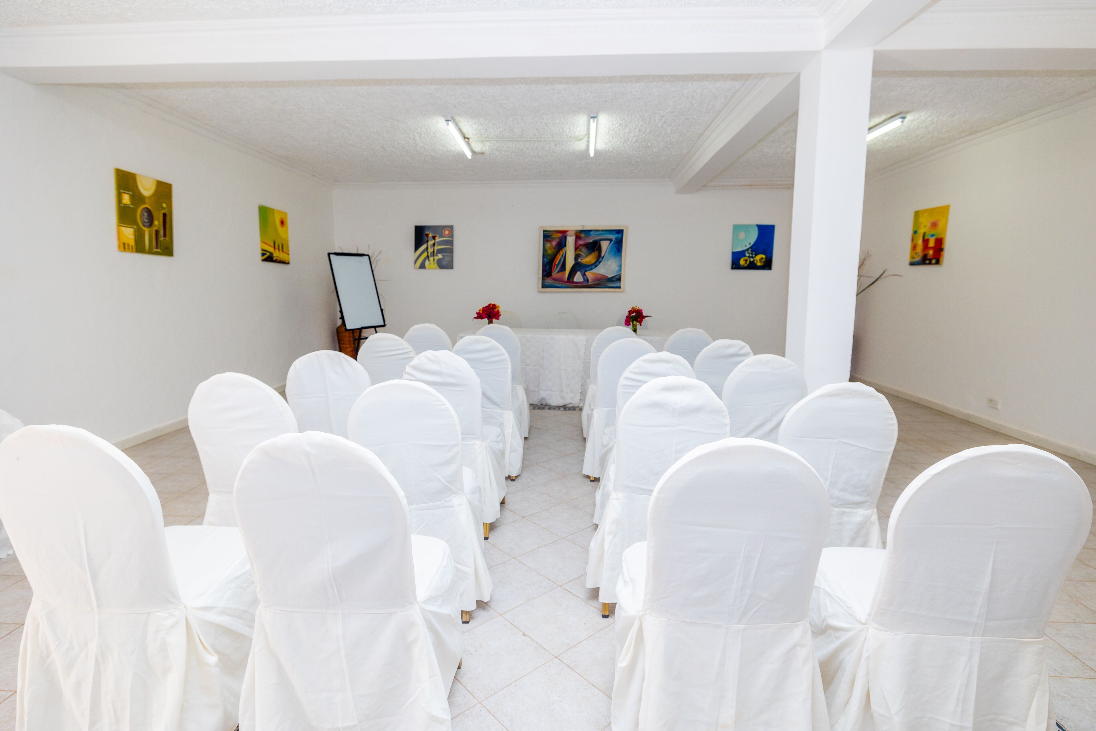 Una sala amb cadires blanques disposades per files, una taula blanca al centre i obra d'art a les parets.