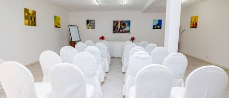 A room with white chairs arranged in rows, a white table in the center, and artwork on the walls.