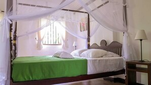 Ein Himmelbett mit einem grünen Überwurf, weißen Kissen und einem weißen Moschee-Vorhang.