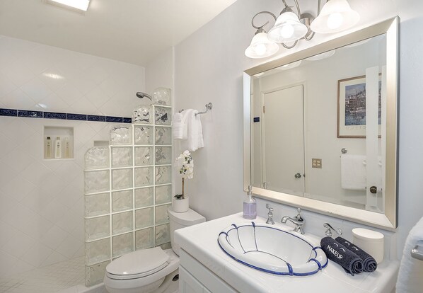 A modern bathroom with a glass shower enclosure, a white sink with a blue accent, and a large mirror above the vanity. - 3914 Pacific Sandpiper ~ Oceanfront Condo, Pool/Spa (Monterey)