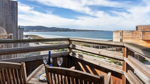 A wooden deck with a table, chairs, and a glass of wine, overlooking a beach and ocean. - 3914 Pacific Sandpiper ~ Oceanfront Condo, Pool/Spa (Monterey)