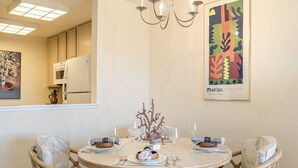 A dining area with a round table, four chairs, a chandelier, and a framed artwork on the wall. - 3914 Pacific Sandpiper ~ Oceanfront Condo, Pool/Spa (Monterey)