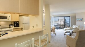 A modern kitchen with a microwave, stove, and coffee maker, leading to a living area with a sofa and a balcony with a city view. - 3914 Pacific Sandpiper ~ Oceanfront Condo, Pool/Spa (Monterey)