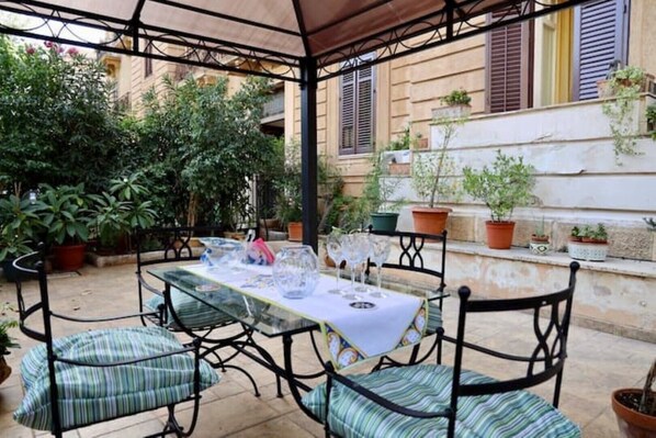 An outdoor patio with a table set for dining, surrounded by potted plants and a covered seating area.