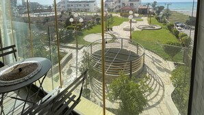 A balcony with a view of a landscaped area, a circular water feature, and buildings in the distance. - Duplex at Solemar resort, totally renovated, pools, tennis, basketball, football (Kaslik)