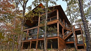 A multi-level wooden cabin with balconies, surrounded by trees.