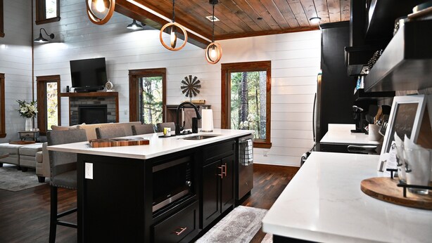 A modern kitchen with a central island, built-in appliances, and a large window overlooking a forest.
