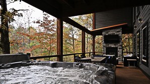 A hot tub area with a stone fireplace, wooden deck, and a view of autumn trees.