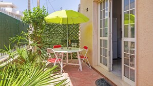 Een terras met een tafel en stoelen, een groene parasol en een schuifdeur naar een keuken.