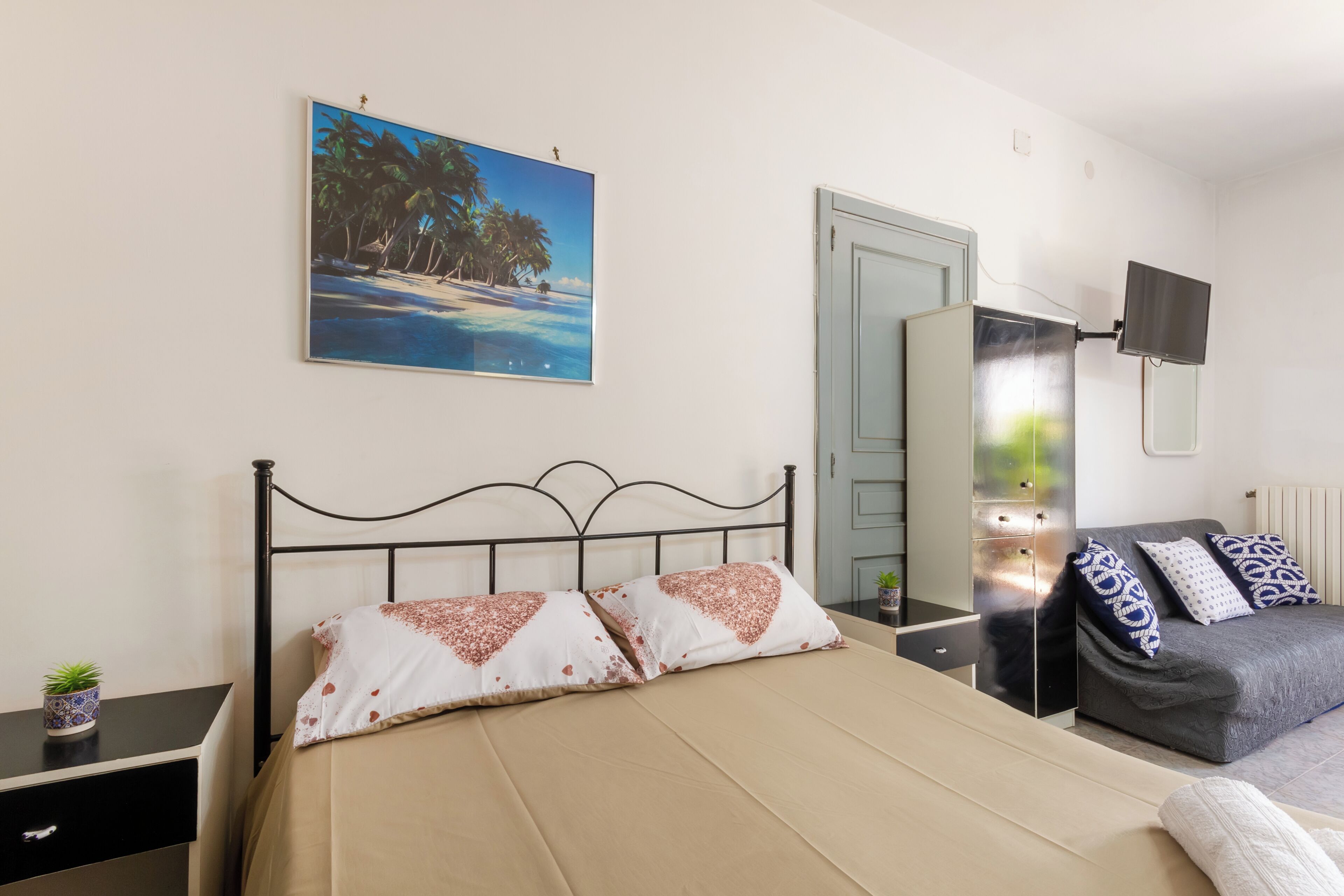 A bedroom with a bed, a sofa, a TV, a painting, and a small plant.