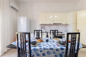 Una mesa de comedor con sillas, una cocina al fondo y un refrigerador blanco.