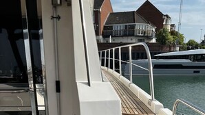 A boat deck with a wooden floor, a metal railing, and a view of a marina with buildings. - Superyacht on 5* Town Quay Marina, Southampton (Southampton)