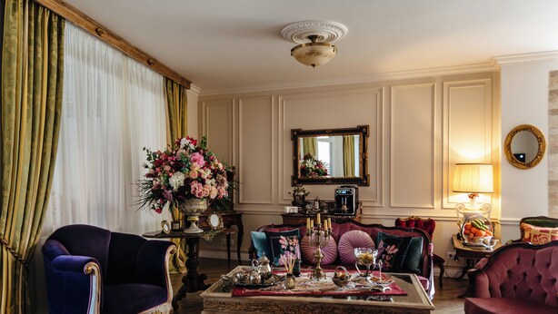A classic room with a plush armchair, a side table with a vase of flowers, and a mirror on the wall. - Ateneea Luxury Rooms (Cluj-Napoca)