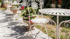 A patio with white metal chairs and tables, surrounded by greenery and a statue. - Ateneea Luxury Rooms (Cluj-Napoca)