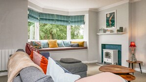 Een gezellige woonkamer met een ingebouwde bank bij een groot raam, een open haard en een kleine tafel.