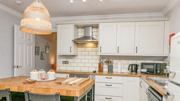 Een moderne keuken met witte kastjes, een houten aanrecht en een hanglamp.