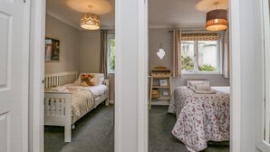 Een slaapkamer met een bed, een bureau en een stoel. Er is een raam met gordijnen en een hanglamp.