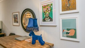 Een houten bureau met een blauwe lamp, een laptop en een boek. Er hangen ingelijste kunstwerken aan de muur.