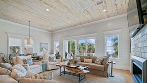 A spacious living room with a high ceiling, large windows, and a fireplace. - Eastern Lake Beach Access, Heated Pool, 6 Seater Golf Cart!! (Santa Rosa Beach)