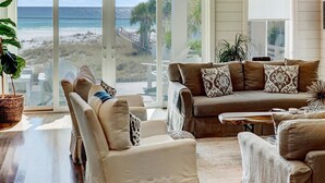 A spacious living room with a large window overlooking a beach, furnished with a beige sofa, armchairs, and a coffee table. - Eastern Lake Beach Access, Heated Pool, 6 Seater Golf Cart!! (Santa Rosa Beach)