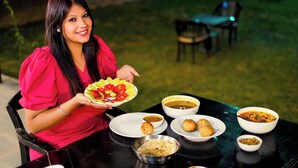 A person seated at an outdoor table with various dishes, including a plate of sliced vegetables, bowls of soup, and other food items. - Jawai Sanderao Farms (Sumerpur)