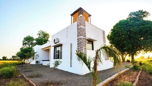 A modern house with a stone chimney, white exterior, and a gravel driveway. - Jawai Sanderao Farms (Sumerpur)