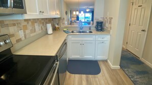 Une cuisine moderne avec des meubles blancs, une cuisinière noire, une machine à café et une vue sur le salon par la fenêtre.