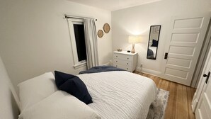 A bedroom with a bed, a nightstand, a lamp, a window with curtains, a mirror, and a door. - Loung Room Retreat - 3 Blocks to Mayo Campus (Rochester)