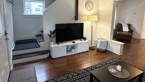 A living room with a staircase, a flat-screen TV, a lamp, a brown leather chair, and a patterned rug. - Loung Room Retreat - 3 Blocks to Mayo Campus (Rochester)