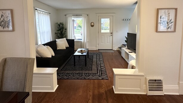 A living room with a black sofa, a coffee table, and a TV. There is a door leading to another room. - Loung Room Retreat - 3 Blocks to Mayo Campus (Rochester)